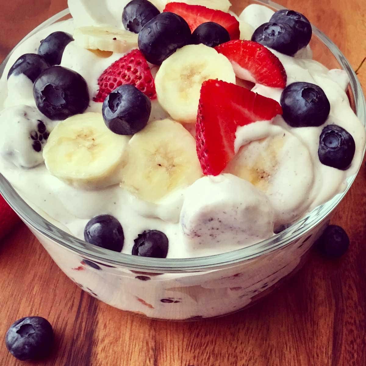 cheesecake fruit salad in a bowl sitting on a wood cutting board surrounded by blueberries