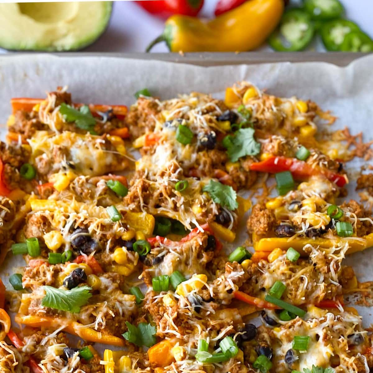  mini pepper nachos sitting on waxed paper topped with meat, cheese, green onions, corn and black beans. 