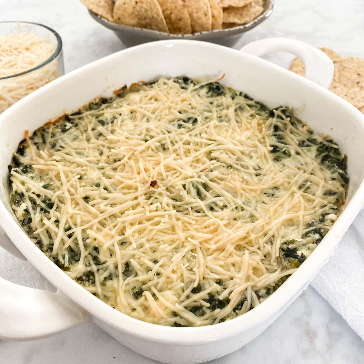 Healthy Spinach Artichoke Dip in a white pan with chips in the background.