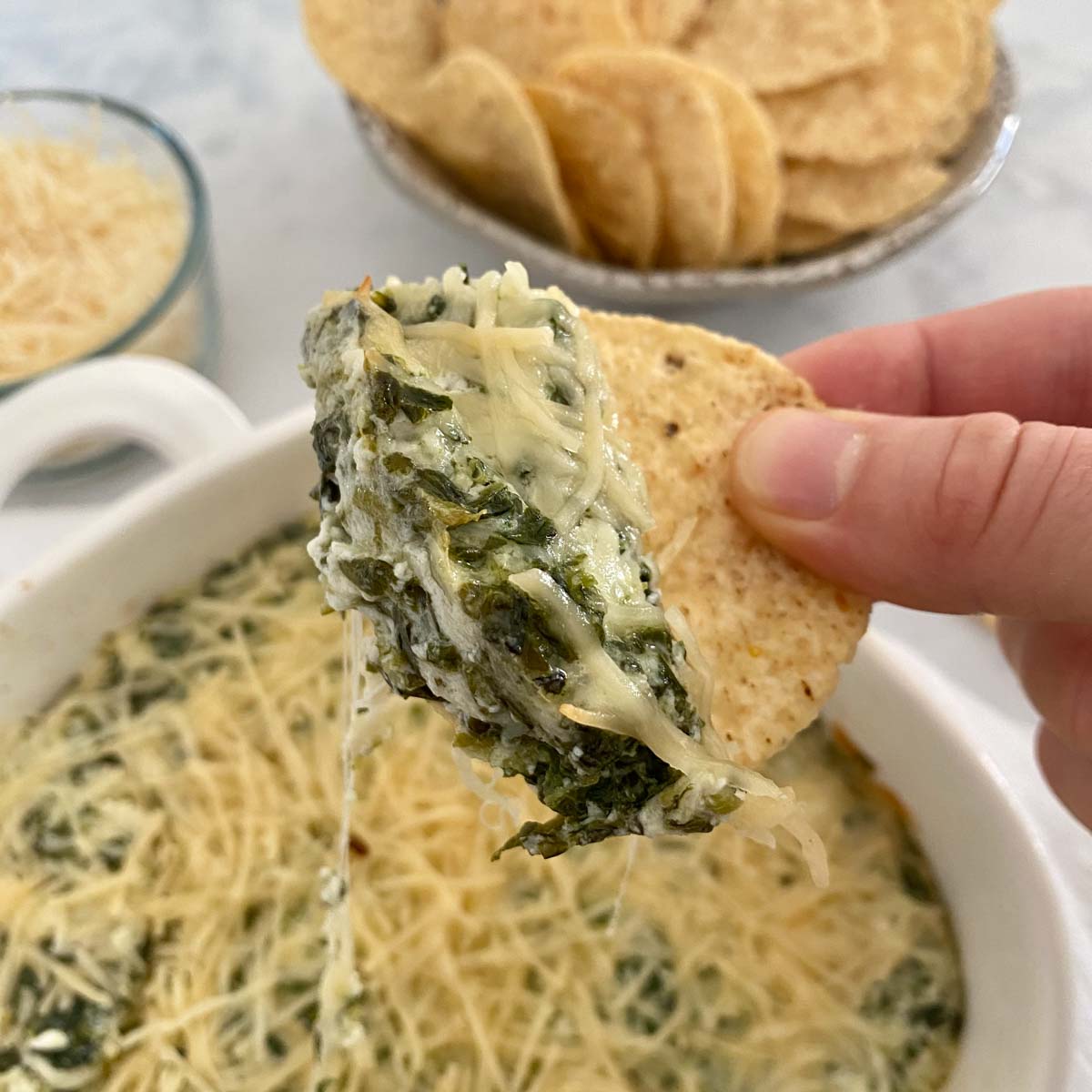 Chip dipping into Healthy Spinach Artichoke Dip.