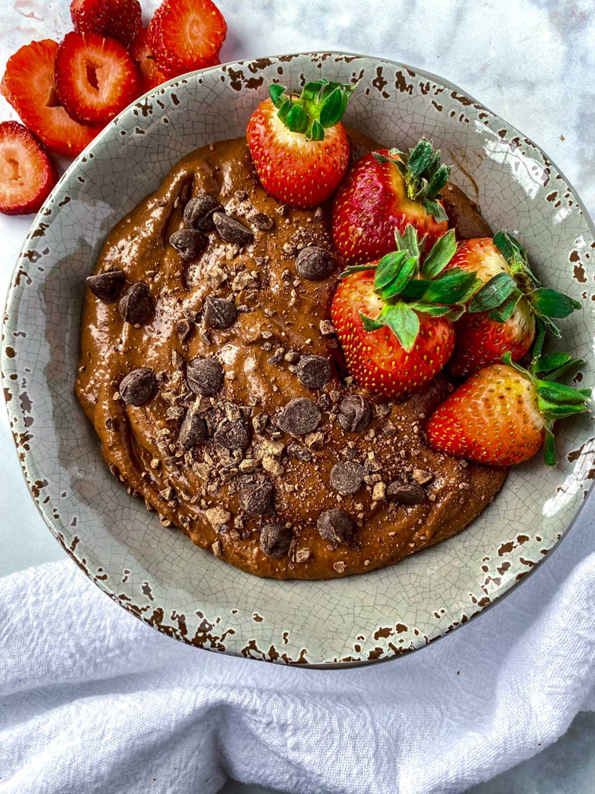 brownie batter hummus in a bowl topped with crushed chocolate, chocolate chips and strawberries.