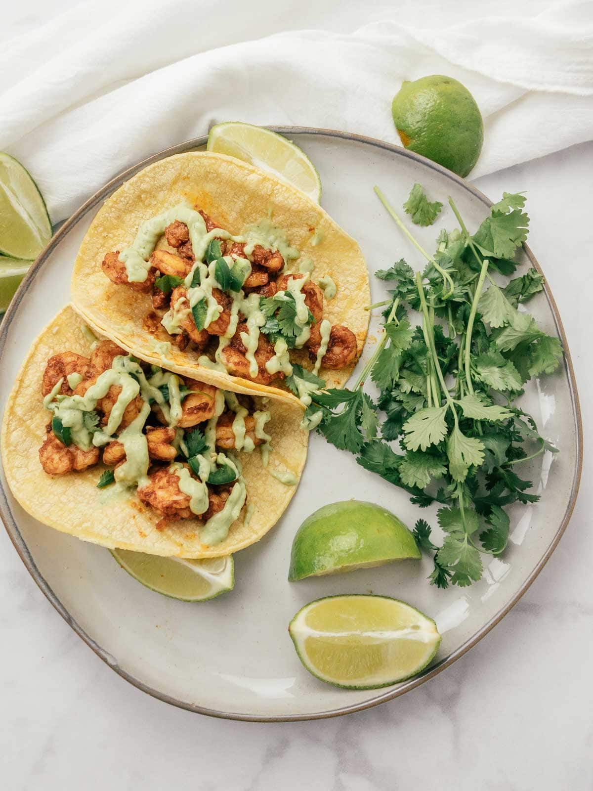 chili lime shrimp tacos on a plate with avocado cream sauce and cilantro and lime on the side. 