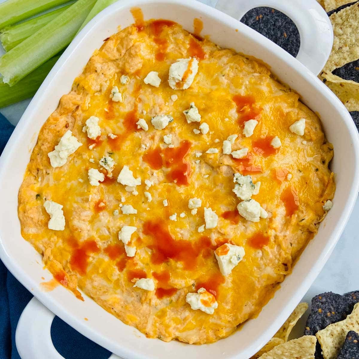 healthy buffalo chicken dip in a pan with celery and chips in the background. 