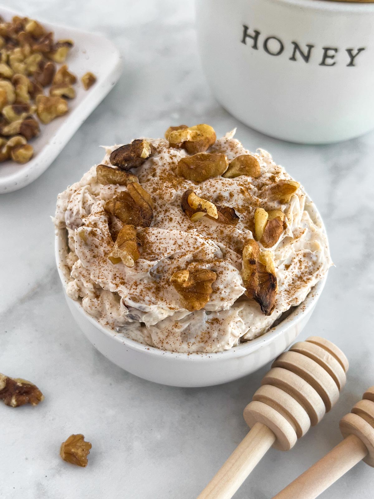 white bowl on a white counter containing honey cream cheese topped with walnuts.