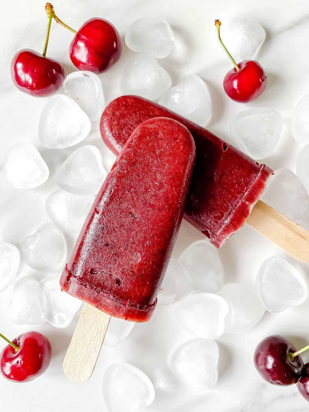 cherry mango popsicles with ice and cherries in the background. 