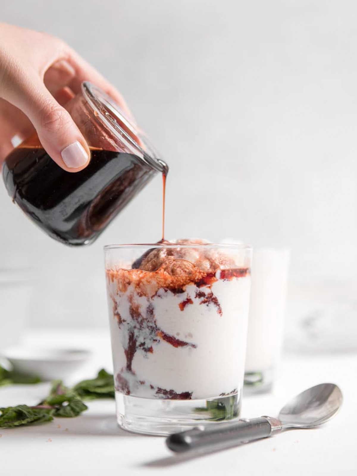 cup of tart cherry sauce getting poured over frozen greek yogurt.