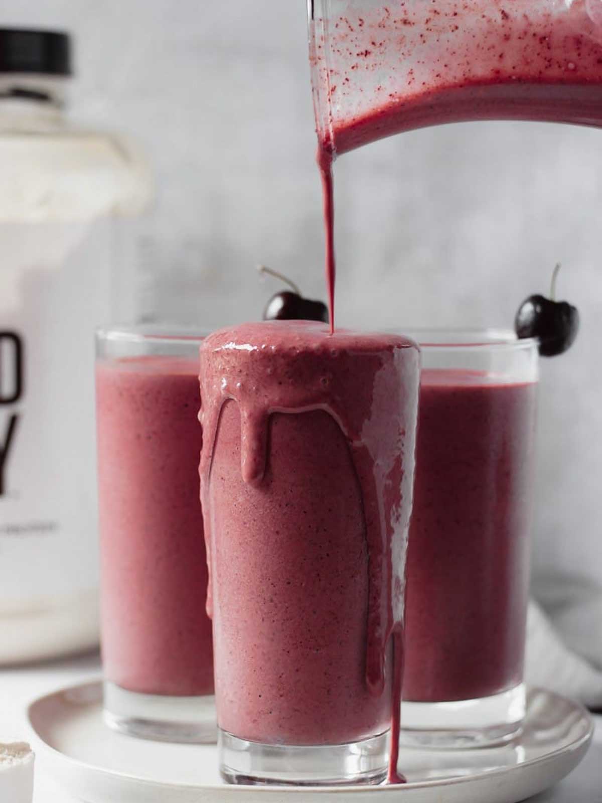 3 glasses of chocolate cherry smoothie getting poured from a pitcher.