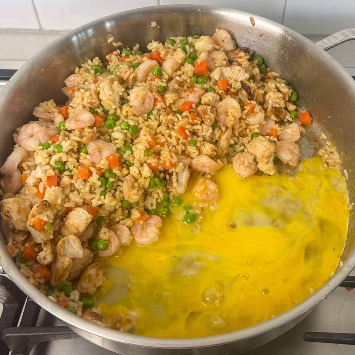 Fried rice on one side of a pan with eggs cooking on the other side.